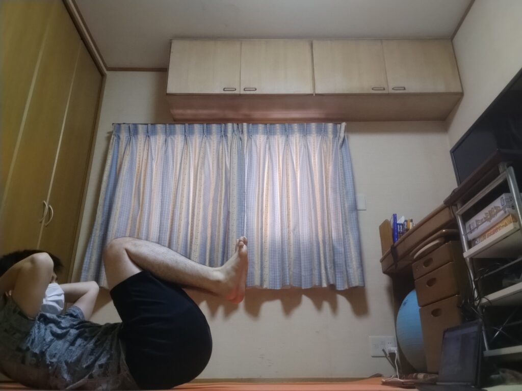 SOELUのオンラインレッスンで腹筋を使うポーズに取り組む男性。自宅でマットの上でトレーニング中。 足を抱える