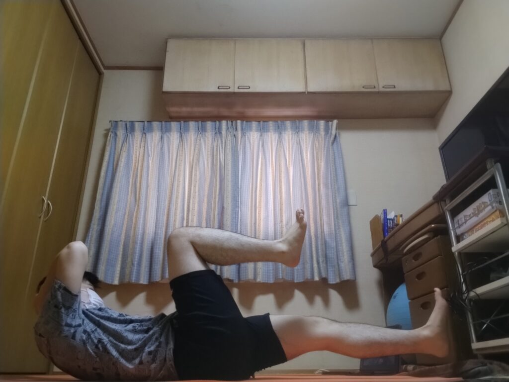 SOELUのオンラインレッスンで腹筋を使うポーズに取り組む男性。自宅でマットの上でトレーニング中。 左にひねる