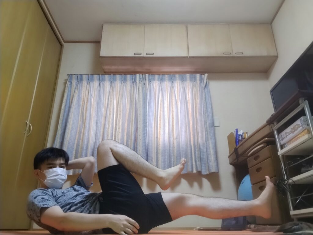 SOELUのオンラインレッスンで腹筋を使うポーズに取り組む男性。自宅でマットの上でトレーニング中。 右にひねる