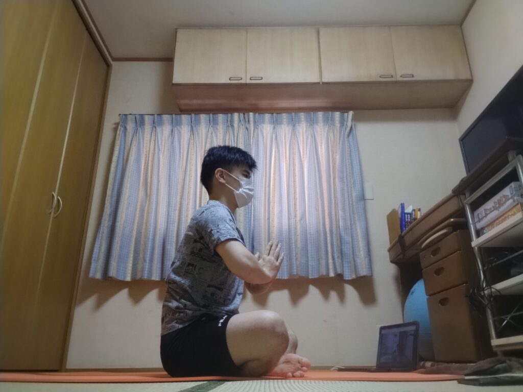 安楽座で姿勢を整えて座る男性。ヨガレッスン冒頭の呼吸を深める準備のポーズ。腕を前に