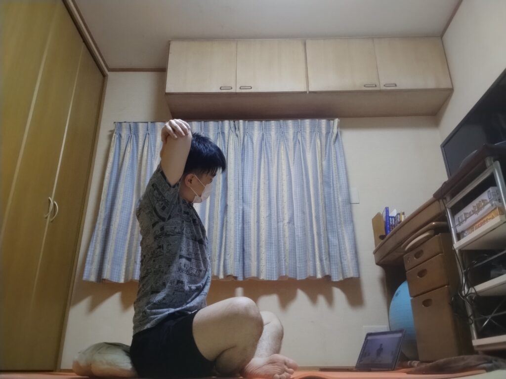 安楽座（Sukhasana）で片腕を頭の後ろに回し肘を押さえるストレッチポーズ