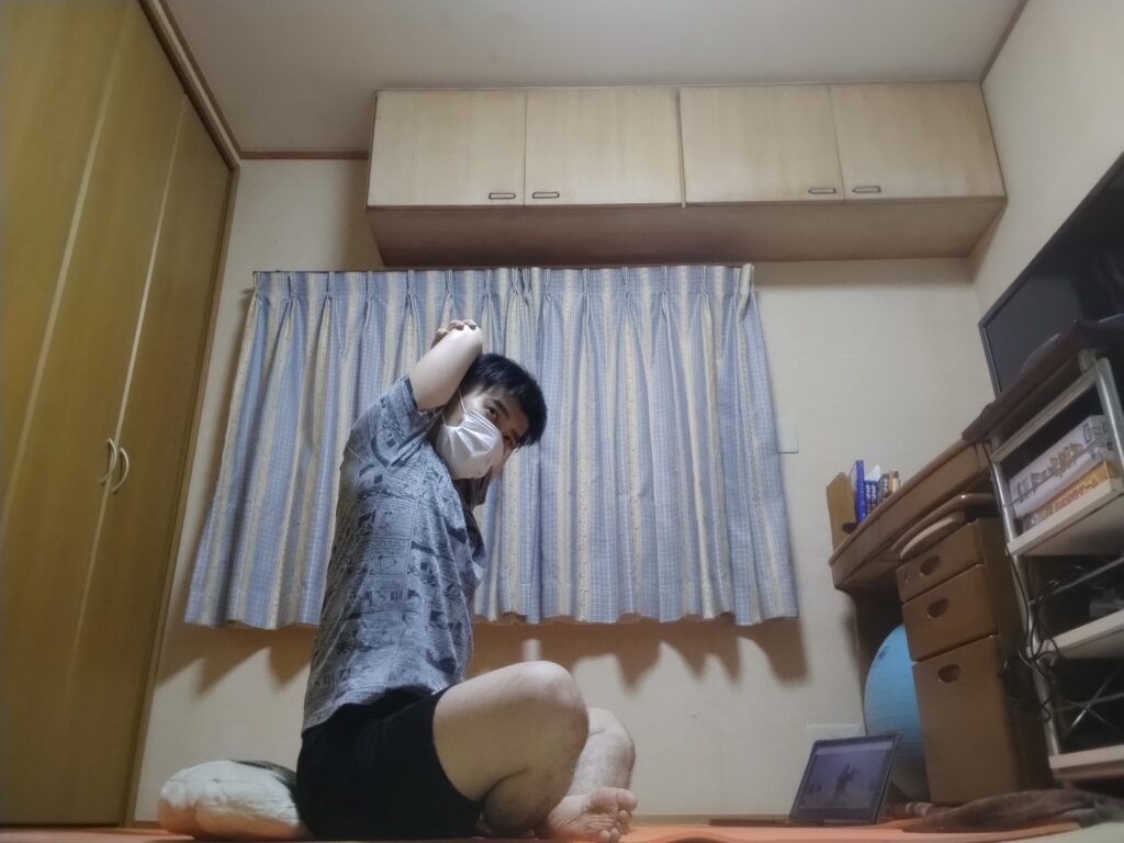 安楽座（Sukhasana）で片腕を頭の後ろに回して肘を伸ばすストレッチポーズ