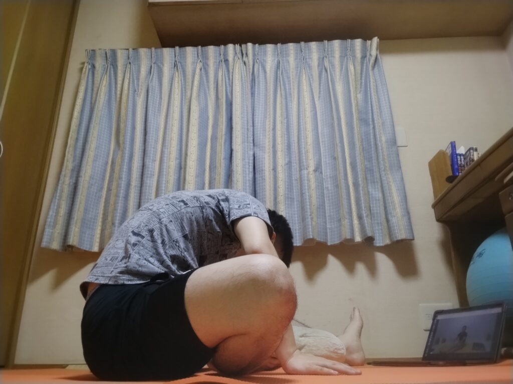 安楽座から前に深く倒れ、腕を床に伸ばしたポーズ