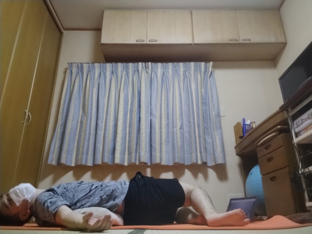 仰向けに寝て右を見て安楽座をとるリラックスポーズ