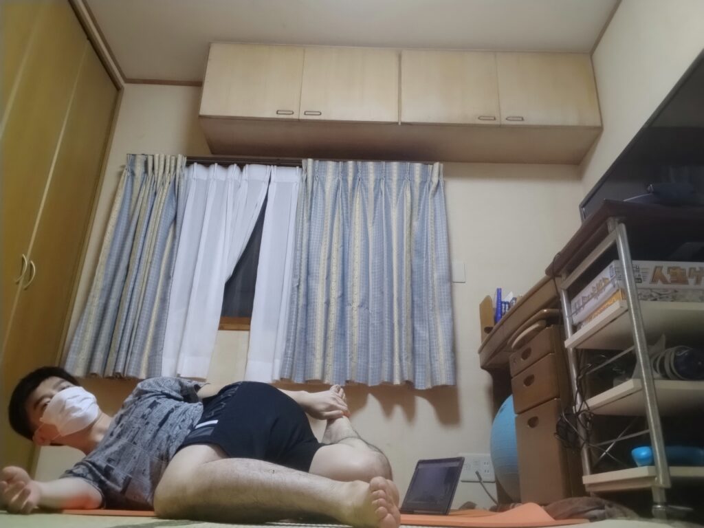 オンラインヨガレッスン中、仰向けでツイストポーズをとる男性。