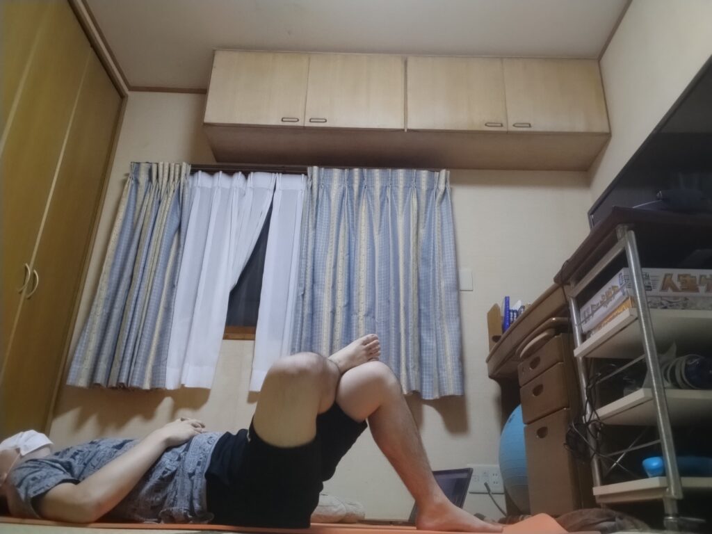 オンラインヨガレッスン後、仰向けで膝を立ててリラックスしている男性。