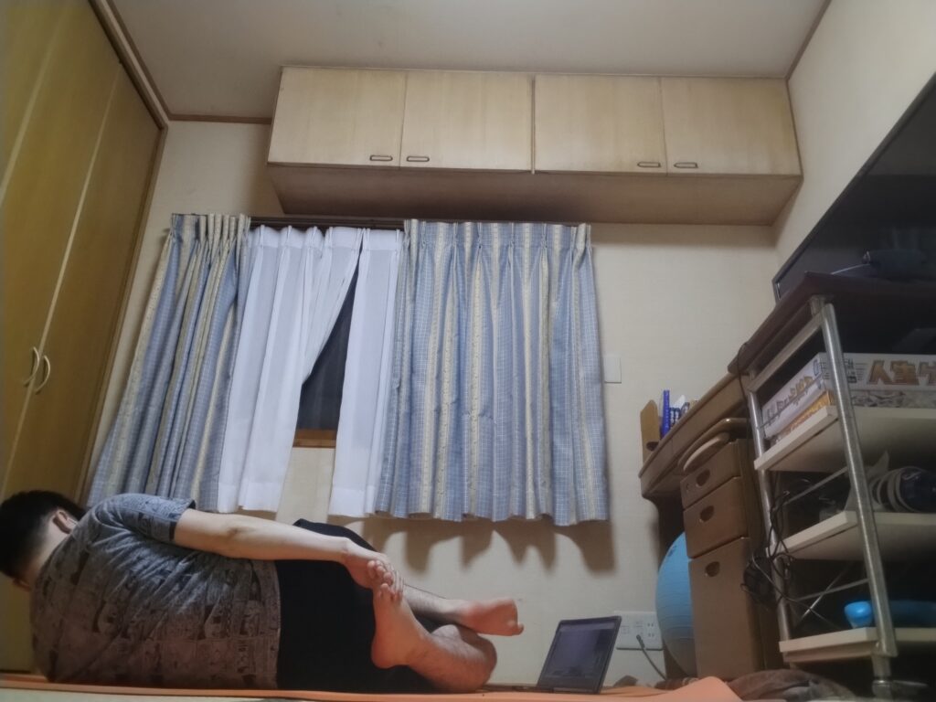 SOELUオンラインヨガでフィギュア4の足を組んだまま、横向きにひねってストレッチしている男性。