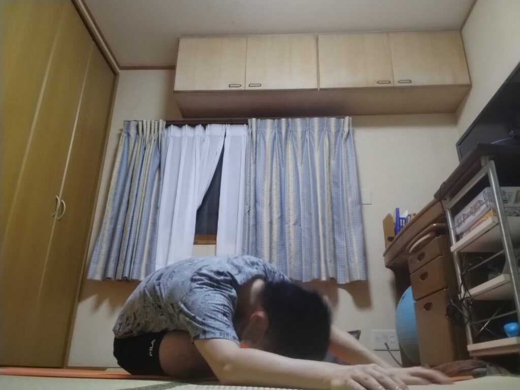 床に座って前屈し、両腕を前に伸ばす男性。ヨガの前屈ポーズを実践中。