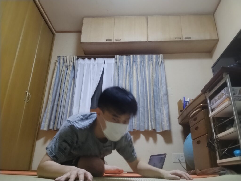 ヨガマットの上でポーズを移行するために体を動かしている男性。オンラインヨガ中。