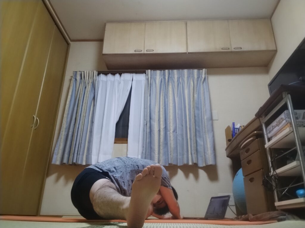 座位の前屈ポーズを横から撮影。オンラインヨガで体を深く倒し、太もも裏を伸ばしている男性。