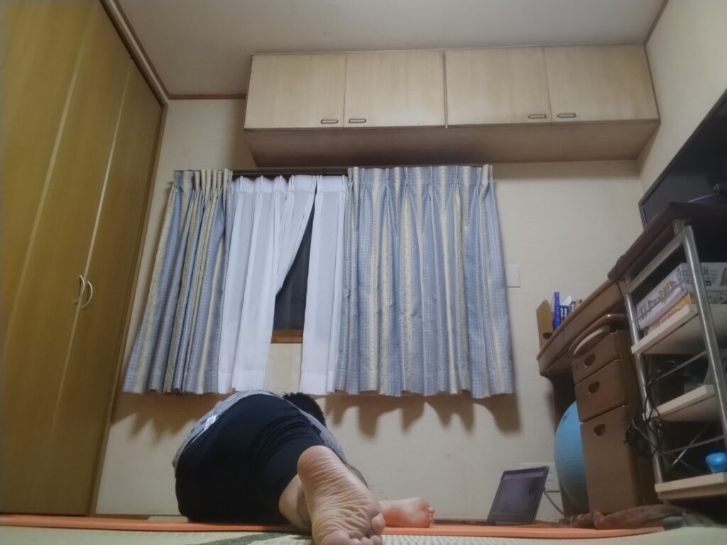 座位の前屈ポーズを後ろから撮影。オンラインヨガで太もも裏を伸ばしている男性の後ろ姿。