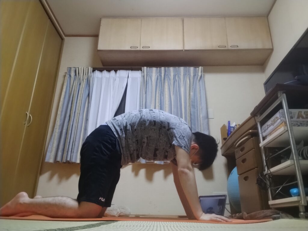 ヨガのキャットポーズで背中を丸め、背骨をほぐしている様子。四つ這いで息を吐きながら背中を高く持ち上げる。