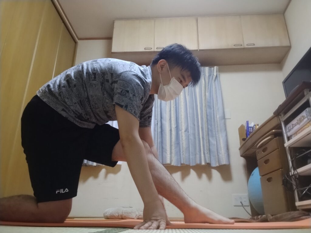 ローランジの準備として片膝立ちで体勢を整える男性。前脚は90度に曲げ、両手は床についている。