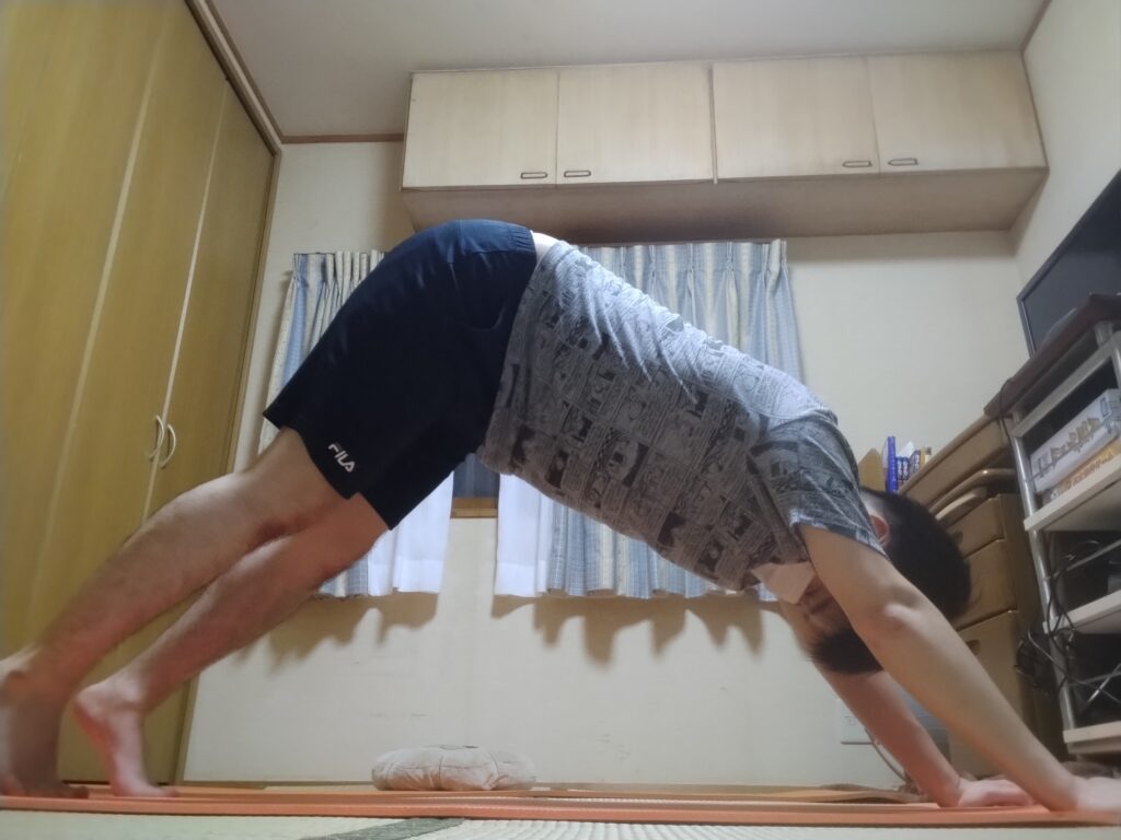 ダウンドッグポーズで両手両足を床につけ、お尻を高く持ち上げて全身を伸ばしている男性。