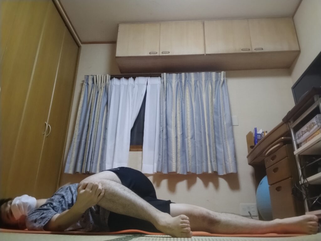 仰向けの状態で片膝をクロスさせてひねるストレッチポーズを行っている男性。背骨のねじれと股関節の柔軟性を高めるポーズ。