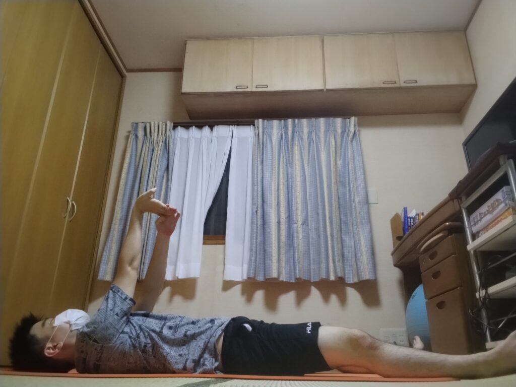 仰向けになりながら腕を天井方向に伸ばし、手首をストレッチしている男性