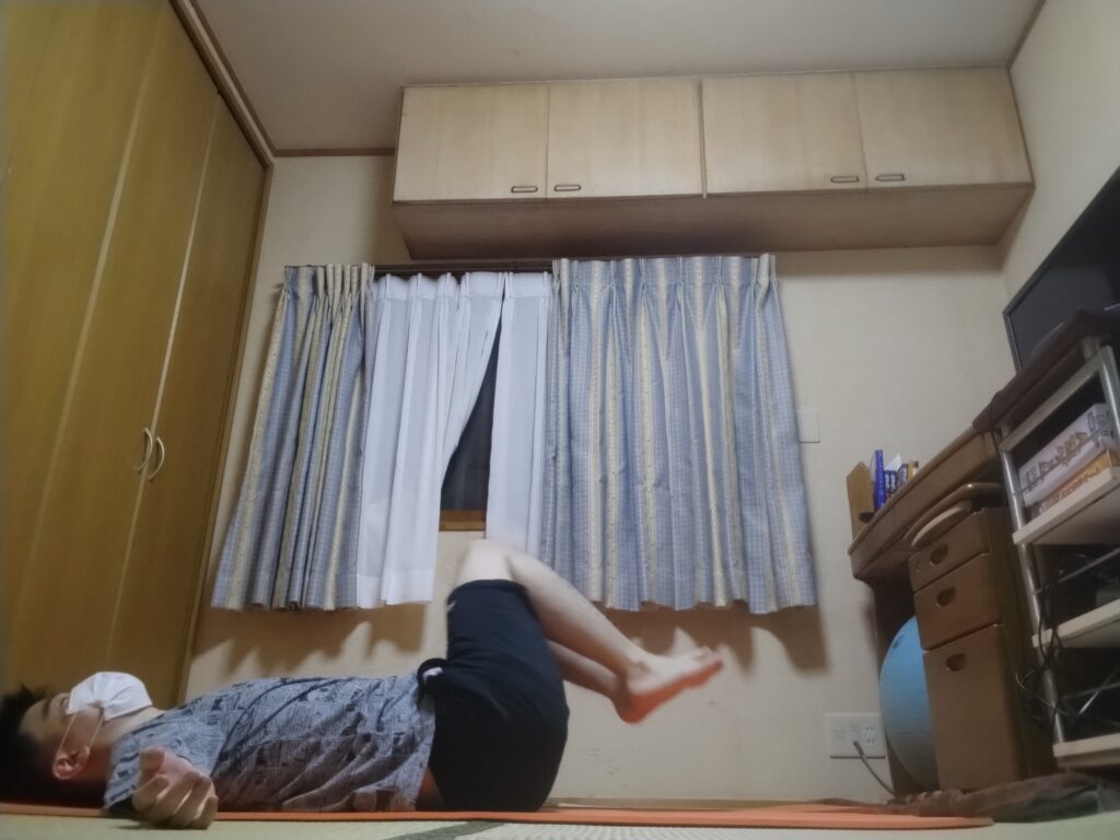 仰向けで両膝を曲げて脚を持ち上げている男性。