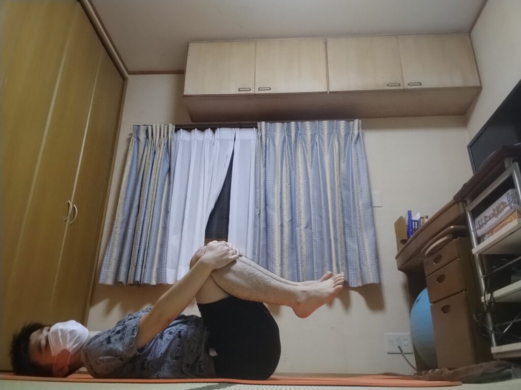 仰向けで両膝を胸に引き寄せて抱えている男性。