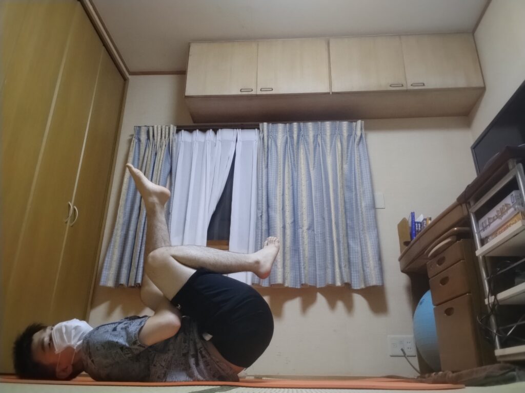 仰向けで片足を反対側の膝に乗せ、ももの裏を抱えてストレッチしている男性。