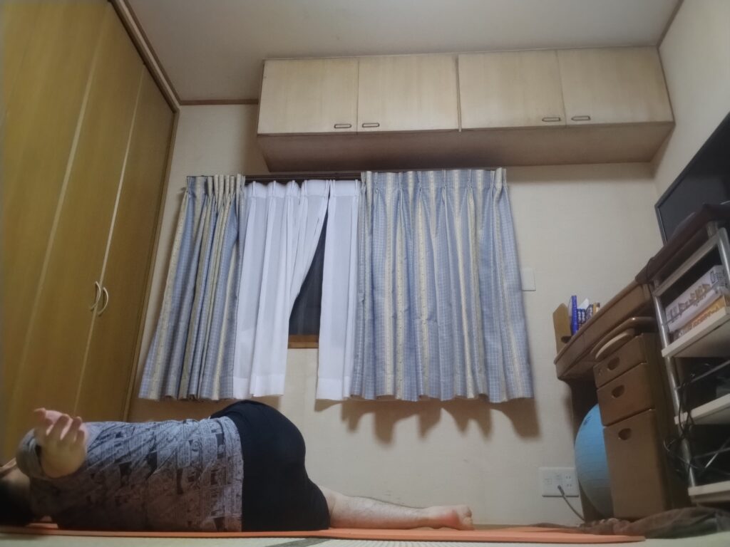 仰向けで両膝を横に倒し、背中と肩を床につけたままツイストしている男性。