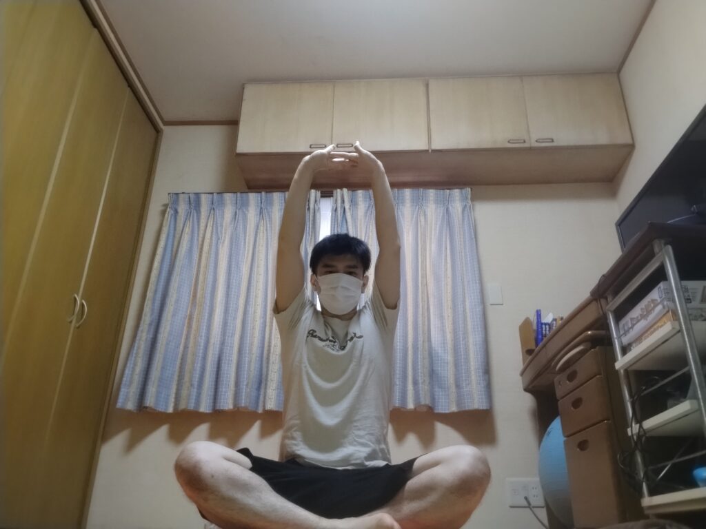 安楽座で腕を上げてストレッチする男性のヨガポーズ