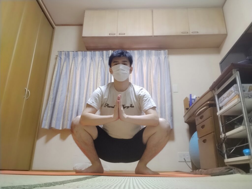 マラーサナのポーズで合掌しながらしゃがむ男性のヨガ姿勢