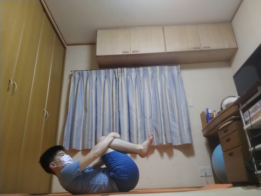 膝を胸に引き寄せて背中を丸める男性のヨガポーズ