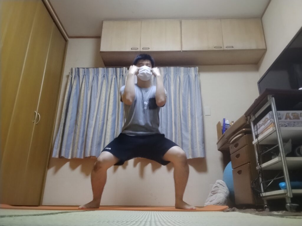 SOELUのオンラインフィットネスでワイドスクワットの姿勢を取り、腕を構えている様子